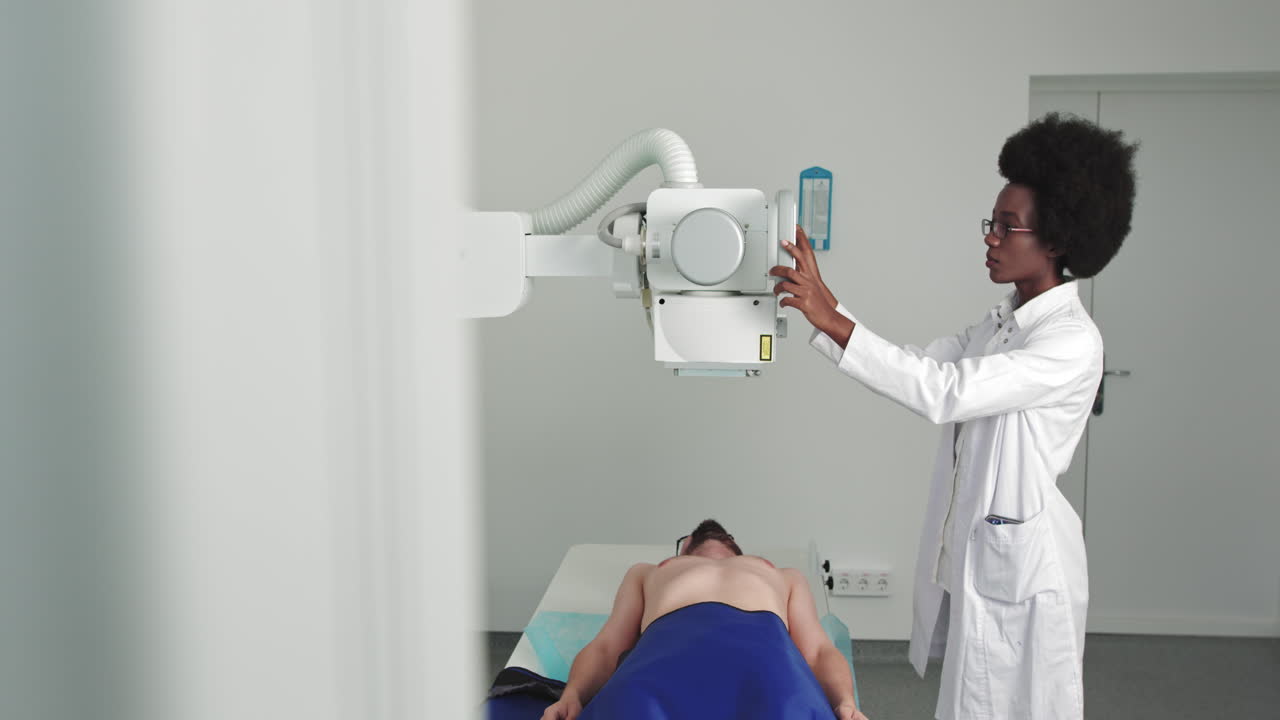 Uomo in ospedale sdraiato su un letto mentre una tecnica esegue una radiografia con una macchina a raggi X alla ricerca di fratture ossee