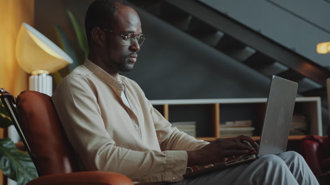 African American Businessman Sitting in Armchair and Using Laptop in Office