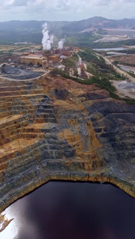 Gold and silver processing facility with deep terraced open-pit and dark mineral runoff water at Barrick Gold mine, Cotuí, Dominican Republic. Vertical drone aerial