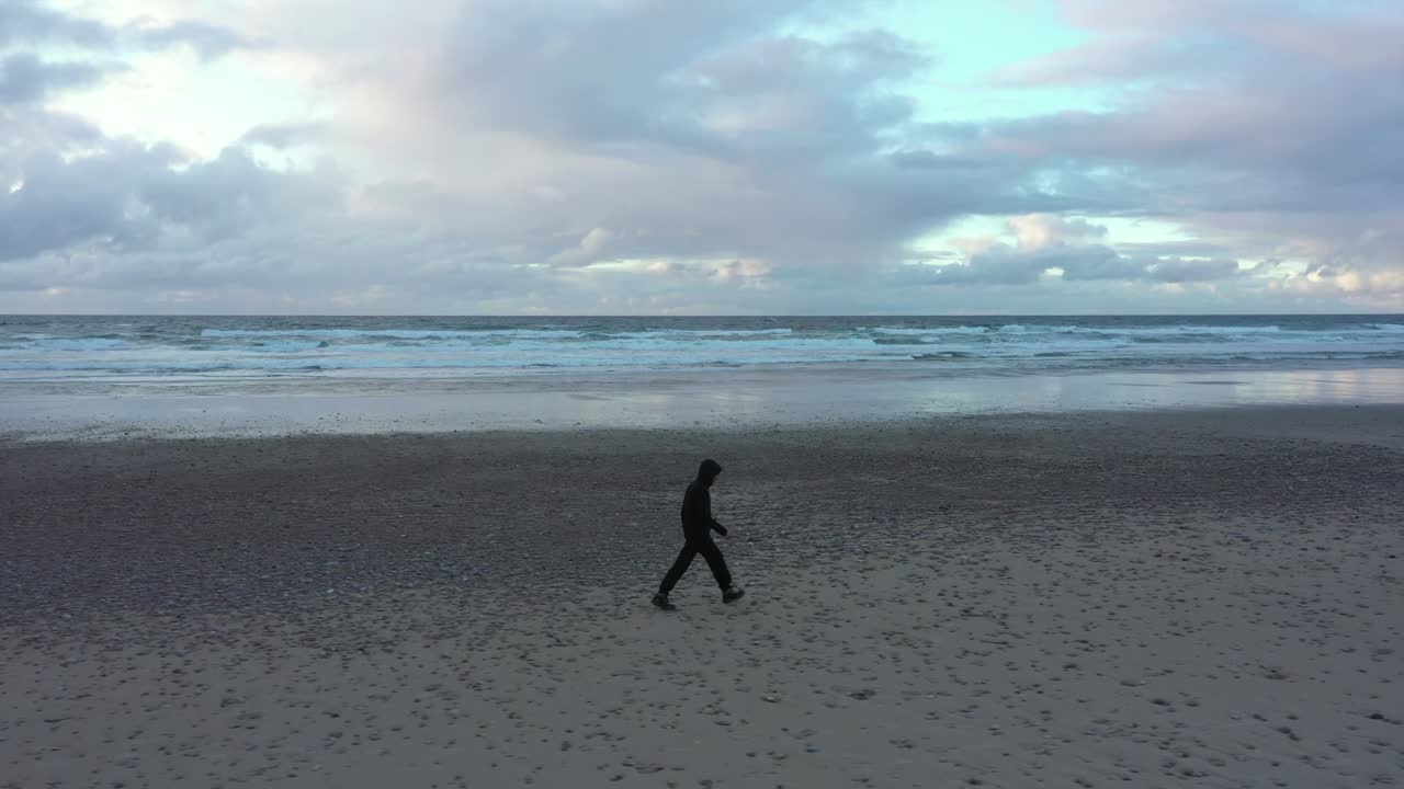 검은 옷을 입은 남자는 몽환적인 하늘이 있는 해변을 홀로 걷는다.