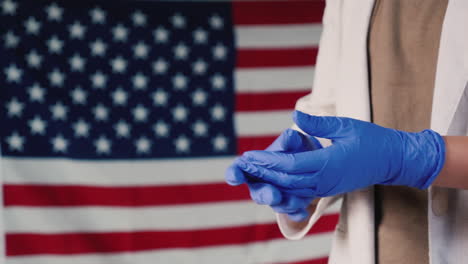 a woman wears protective rubber gloves against the background of the american flag