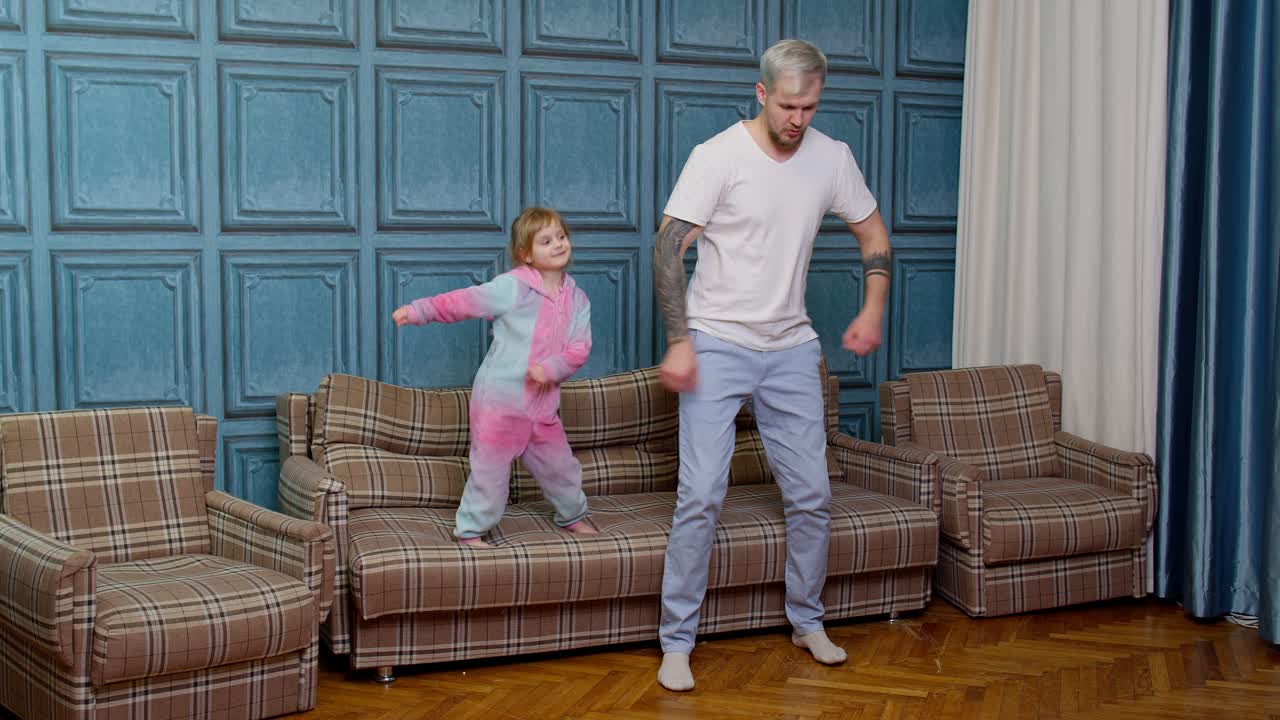 Junger Vater und kleine Tochter springen und tanzen auf dem Sofa im Wohnzimmer eines modernen Hauses.