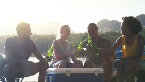 grupo de amigos con mochilas en una camioneta en un viaje por carretera bebiendo cerveza de un refrigerador en el lago