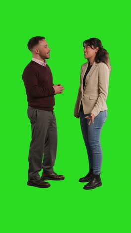 vertical video studio shot of smiling male and female teachers or businesspeople talking before looking at camera against green screen