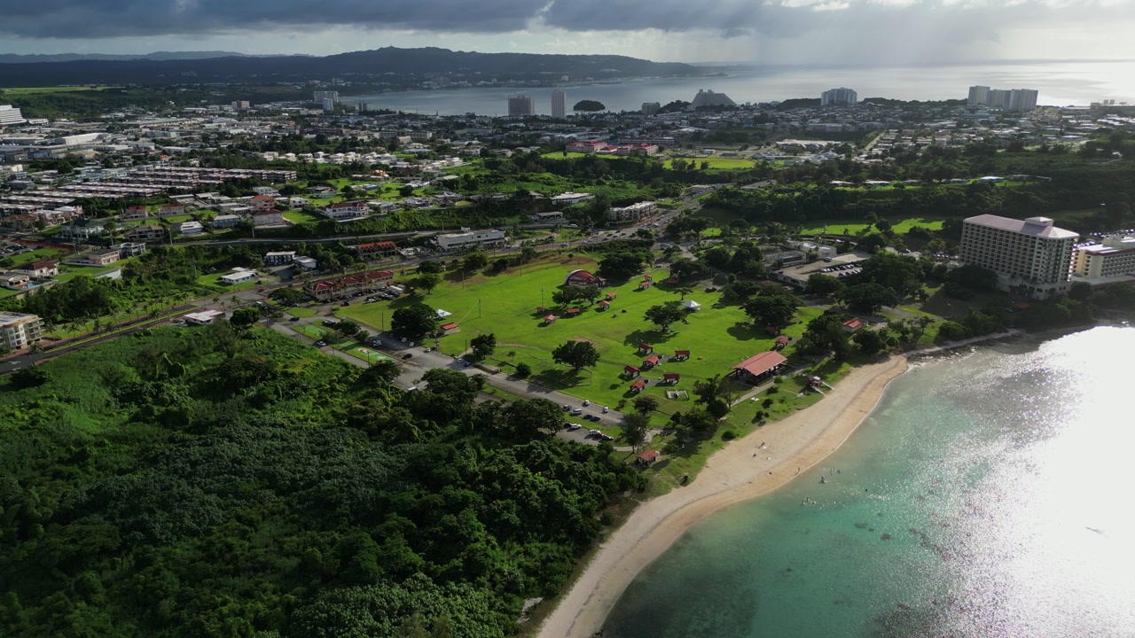 Aerial flyover shot of idyllic public Ypao Beach Park amid lush greenery facing coastal beach waters at Guam, USA.