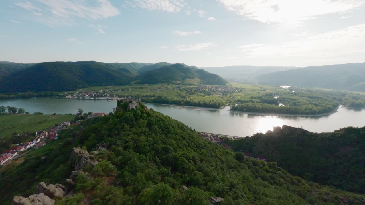 Vue FPV d'un homme debout sur un rocher de montagne, survolant une vallée verdoyante. La personne est au sommet du monde, avec le Danube en arrière-plan. Prise de vue aérienne rapide, spectaculaire et cinématographique, en Autriche.