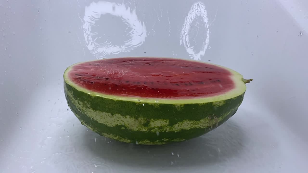물의 제트가 잔한 은 익은 수박에 떨어지고 반으로 잘라서 스프레이를 떨어뜨립니다.
