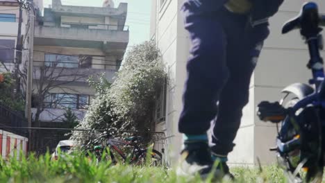 Vista-Desde-El-Suelo-De-Un-Niño-Caucásico-Empujando-Su-Bicicleta,-Hierba-En-Primer-Plano-Borroso-120fps