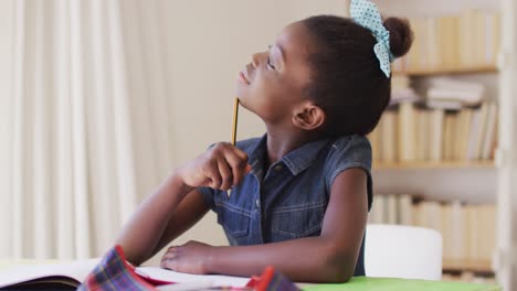 Afroamerikanisches-Mädchen-Hält-Einen-Bleistift-In-Der-Hand-Und-Schaut-Aus-Dem-Fenster-Und-Macht-Hausaufgaben,-Während-Sie-Auf-Dem-Sofa-Sitzt