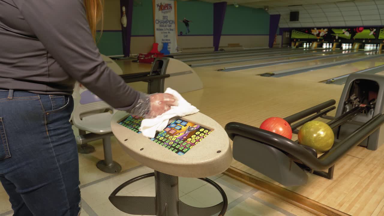 Giovane donna pulisce la segnapunti elettronica in una pista da bowling durante la pandemia.