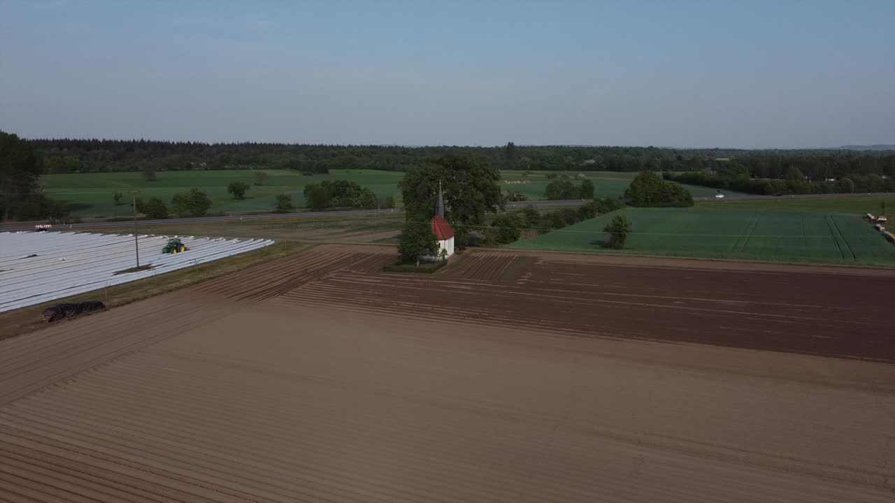 Drone flying high over farmed fields of Asparagus in Germany Western Europe on a sunny day with small Chapel in the back