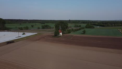 drone flying high over farmed fields of asparagus in germany western europe on a sunny day with small chapel in the back