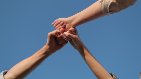 Three friends are banging their fists against the blue sky. Gesture of celebration and joy in teamwork