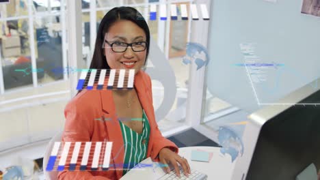 Animation-of-globes,-graphs,-computer-language,-overhead-view-of-asian-woman-working-on-desktop