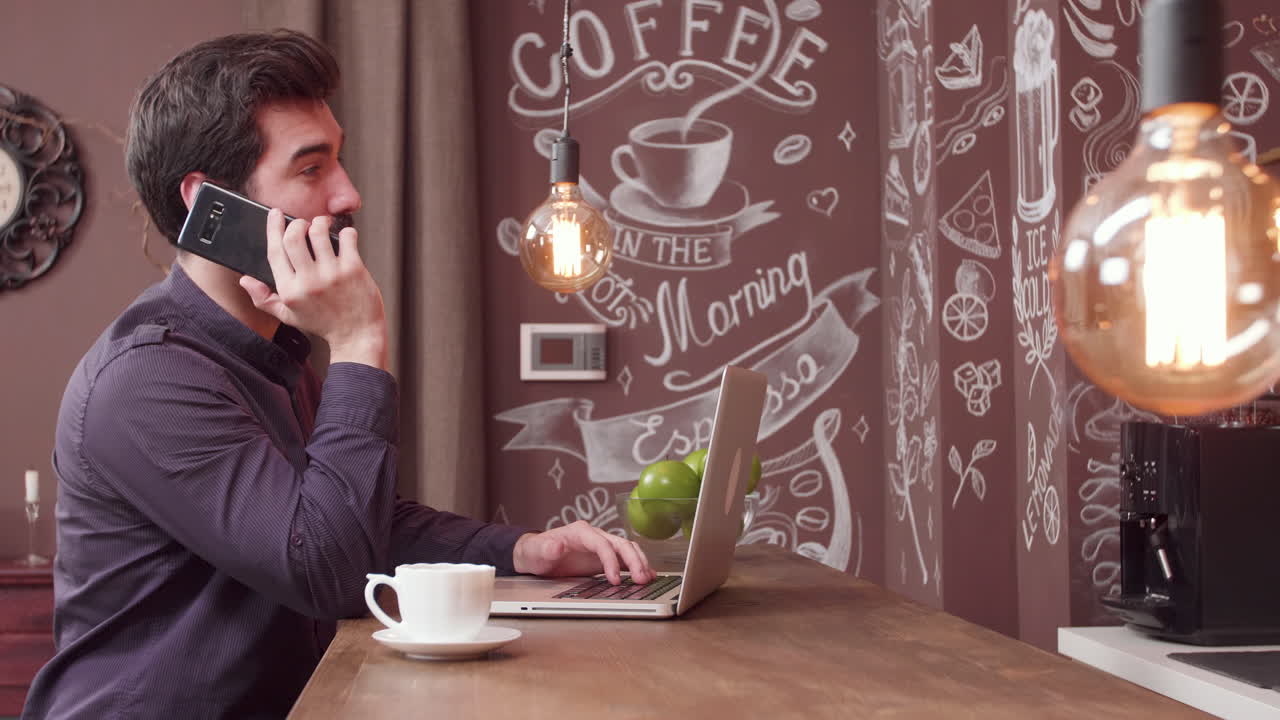 Man working on laptop and talking on phone in cafe