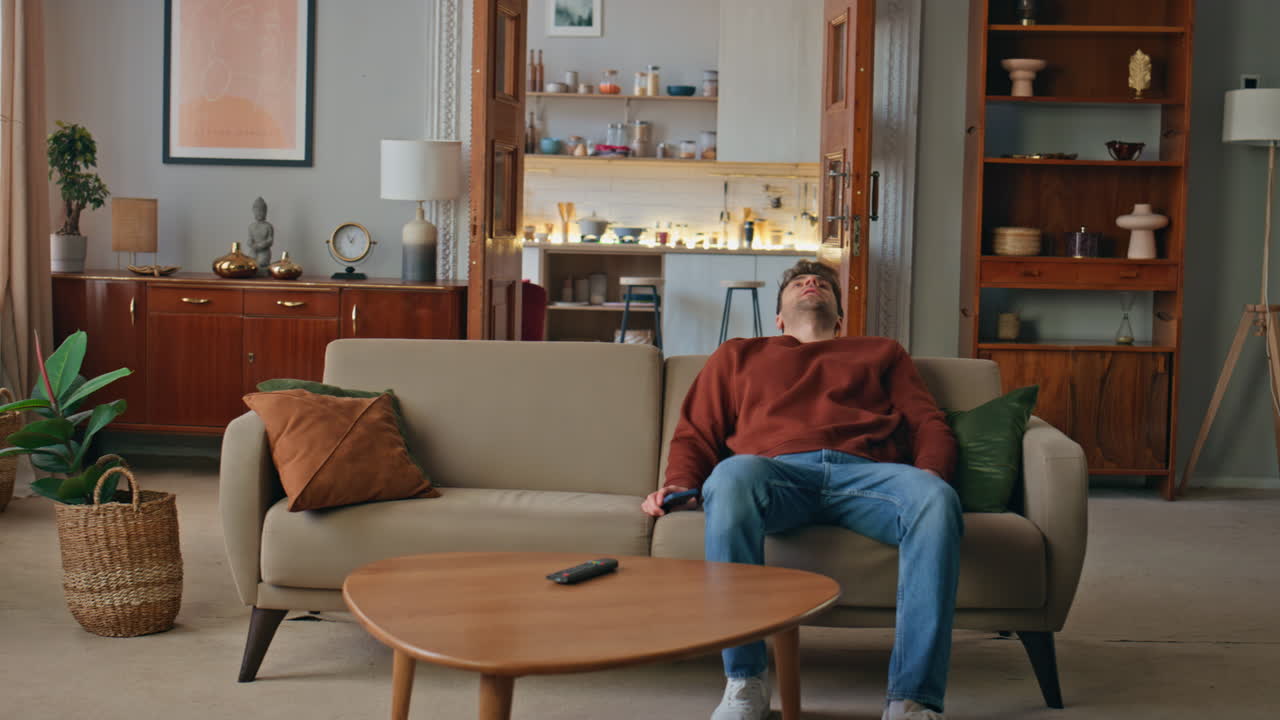 Tired guy sit down comfortable couch home. Exhausted man looking on smartphone