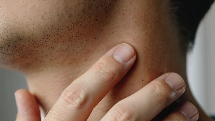 Uomo che si sente la barba incolta, posizionando le dita sul lato sinistro del collo nel bagno di casa, premendo e ispezionando i pori.