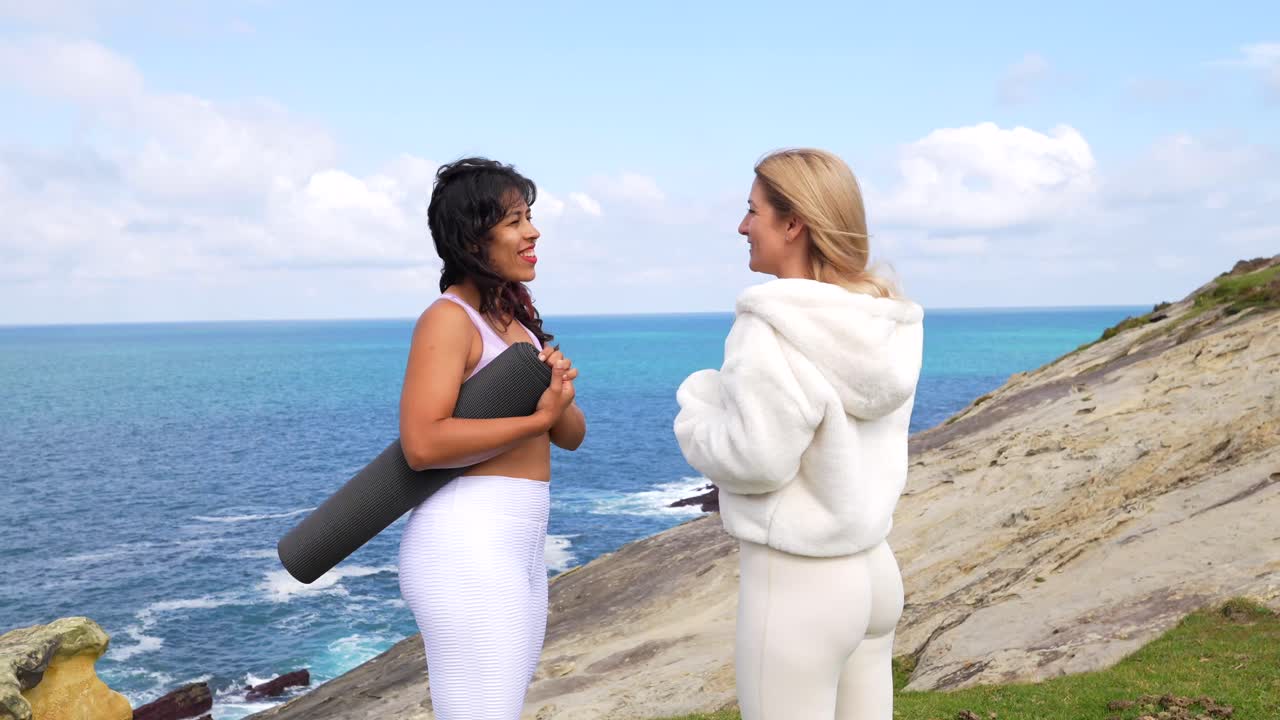 Due donne che parlano in riva all'oceano con un tappetino da yoga