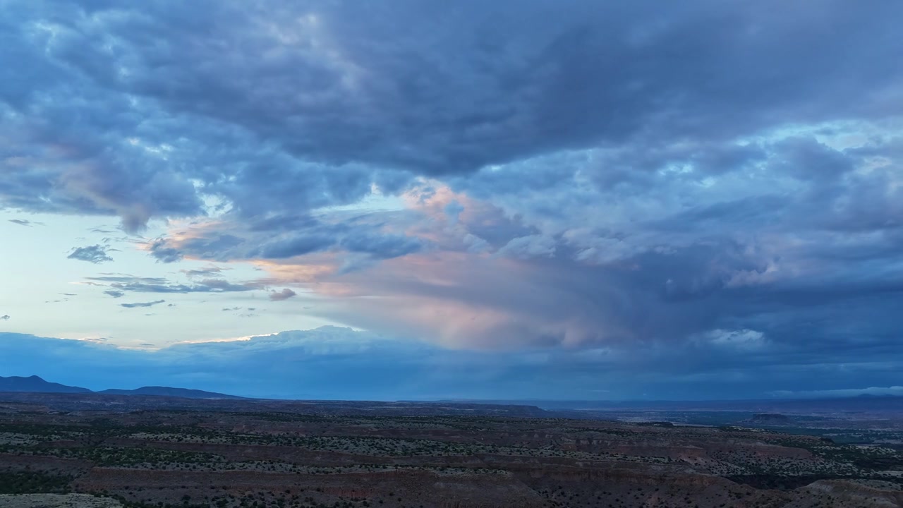 4K UHD drone-timelapse, der fanger det falmende lys fra den gyldne time, som rammer et stemningsfuldt skydække efter en storm. Regnsøjler driver hen over de skyggefulde, barske ørkenplateauer i det sydvestlige USA.