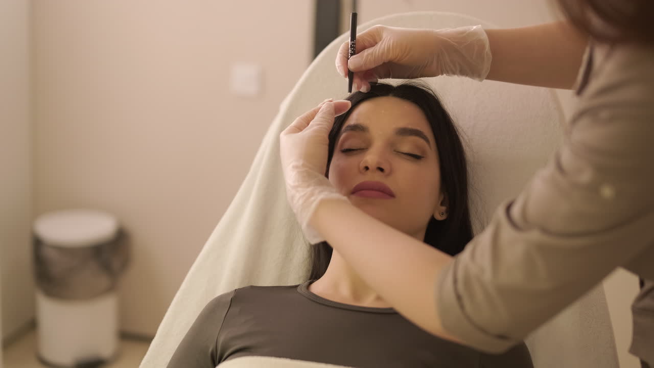 Beautician Marks Young Woman's Eyebrows for Cosmetic Treatment