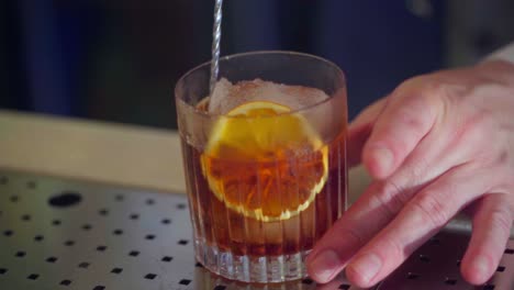 revolviendo suavemente un cóctel con hielo y una rodaja de naranja
