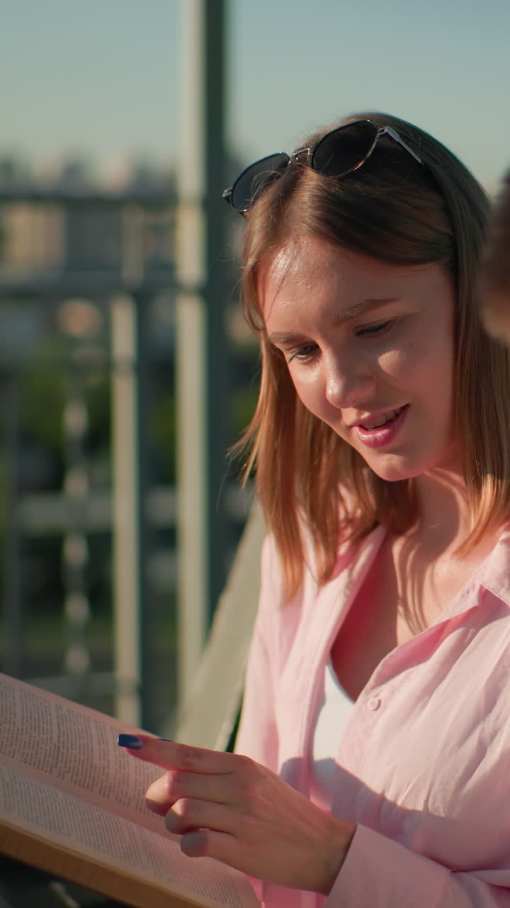 крупный план молодой женщины, показывающей страницы из своей книги своему другу на открытом воздухе, в то время как он выглядит отвлеченным, на заднем плане размытые городские пейзажи, зелень и машины, движущиеся в солнечном свете