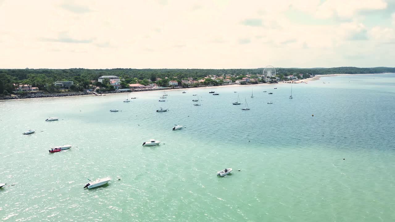A wide drone shot gliding above the Atlantic Ocean, revealing boats scattered along the shimmering water with the coastline of Ronce-les-Bains stretching in the background
