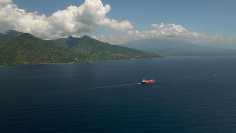 High-angle-aerial-dolly-toward-red-tanker-ship-cruising-in-ocean-near-shoreline