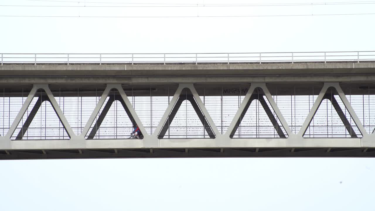 하늘에 있는 철교를 건너 오른쪽에서 왼쪽으로 운전하는 두 명의 자전거 타는 남자, 낮은 관점에서 캡처