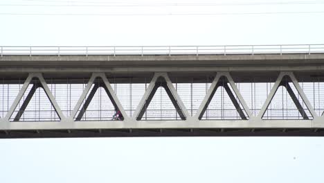 two bike riding men driving from the right to the left over a steel construction bridge in the sky, captured from lower perspective