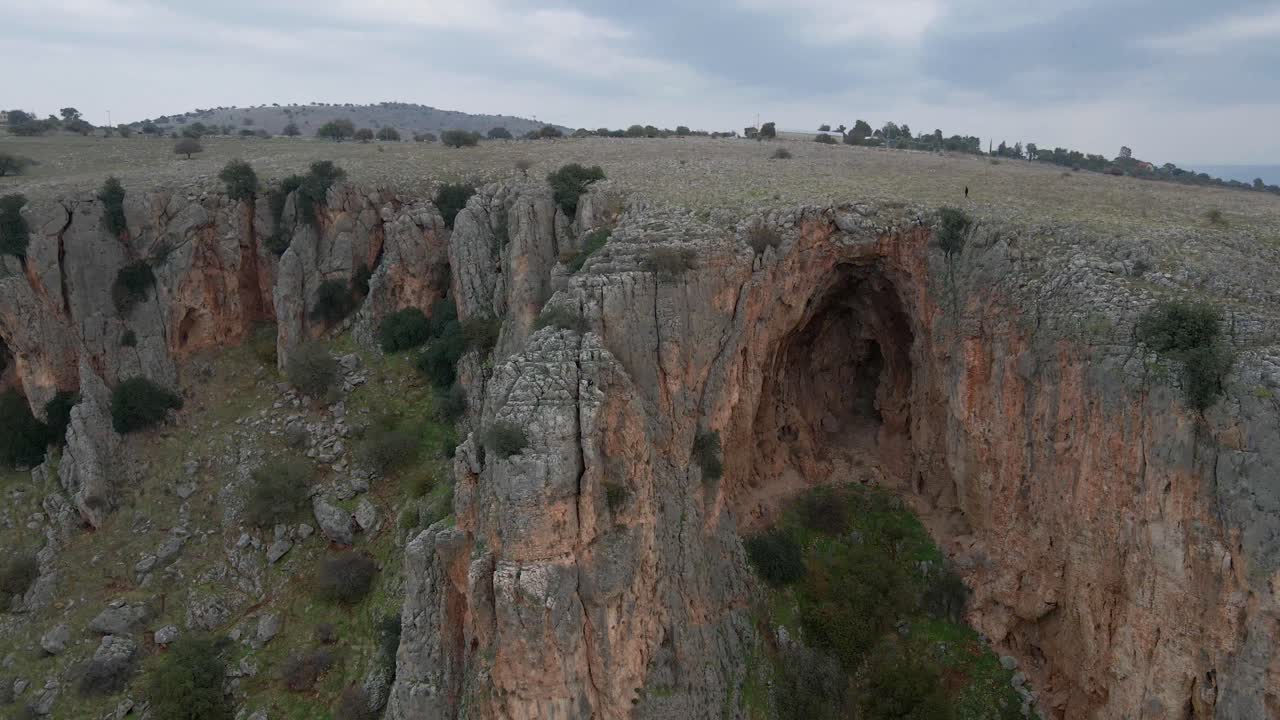 imágenes de drones de un hombre en la distancia caminando sobre un acantilado rocoso y una cueva, israel