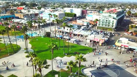 drone volador sobre un día soleado en venice beach california palmeras, parque de patinaje, bicicletas, ciudad y gente