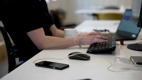 a person typing on a keyboard at a modern office desk with a smartphone and mouse nearby