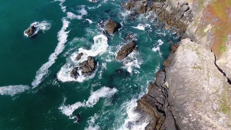 vídeo aéreo de cima capturando a beleza de uma costa rochosa azul com ondas quebrando suavemente contra uma costa acidentada na baía de bodega, costa de gualala, califórnia