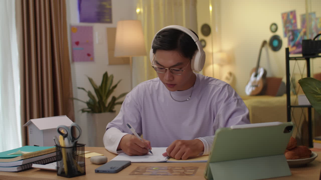 Teenage Student Wearing Headphones Doing Homework at Desk