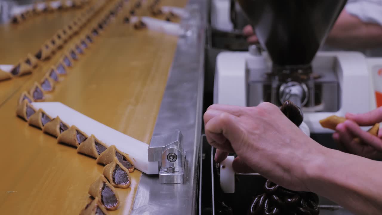 Conveyor belt carrying rows of chocolate-coated triangular pralines with worker operating machinery