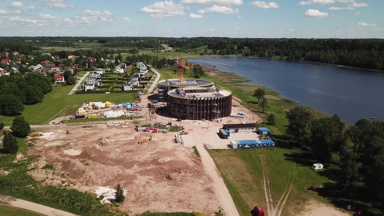 Tomada de drone em pedestal subindo verticalmente ao lado do canteiro de obras do novo complexo de spa moderno, revelando arquitetura de concreto, estruturas de construção e guindaste