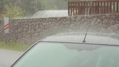 Heavy-rain-and-hail-storm-over-vehicle-roof-and-street,-weather-event-at-village-street