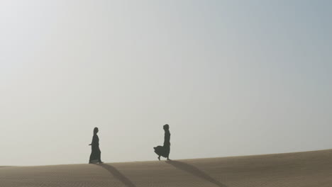 Toma-Extrema-De-Dos-Mujeres-Musulmanas-Con-Vestido-Negro-Tradicional-Y-Hiyab-Caminando-En-Un-Desierto-Ventoso-1