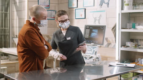 vet using tablet and speaking with woman in clinic