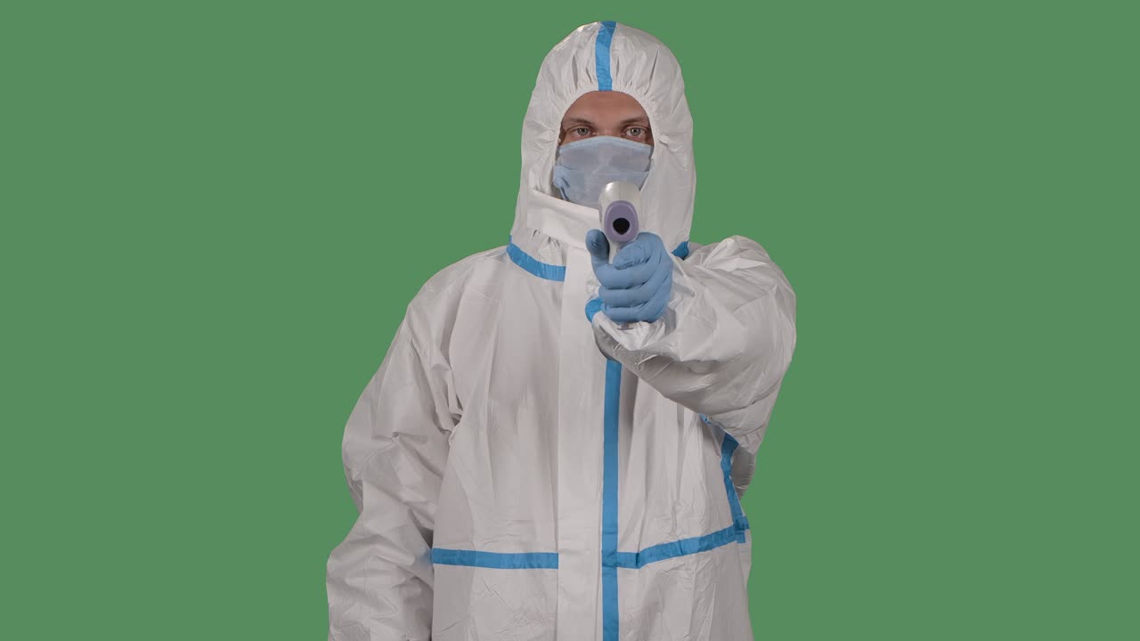 retrato de un hombre con un traje de protección y una máscara médica mira a la cámara con un termómetro sin contacto en la mano y mide la temperatura. pantalla verde, tecla de croma. cámara lenta. primer plano