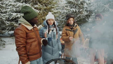 friends eating roasted marshmallows on picnic in winter forest