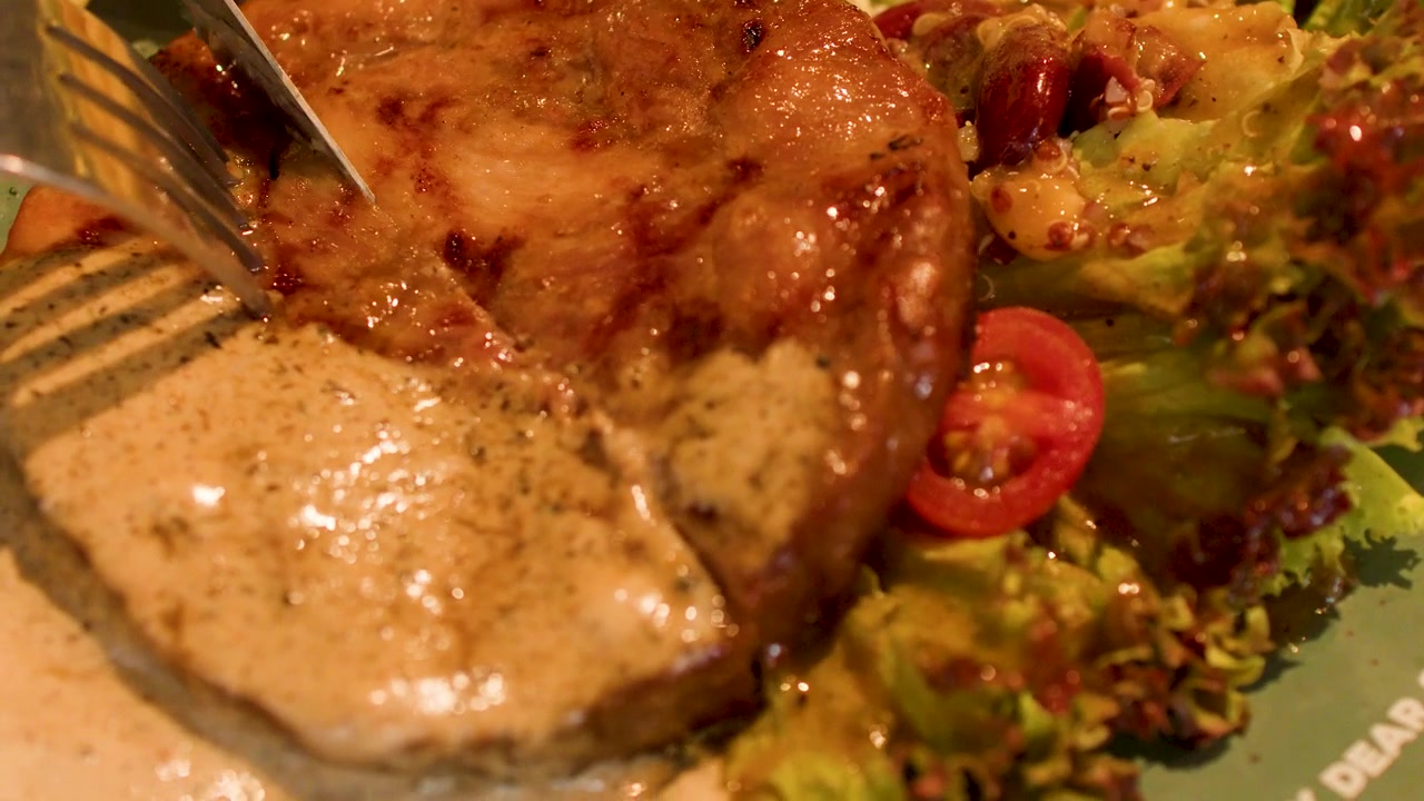Una persona usa un coltello e una forchetta per tagliare una bistecca alla griglia servita con insalata.