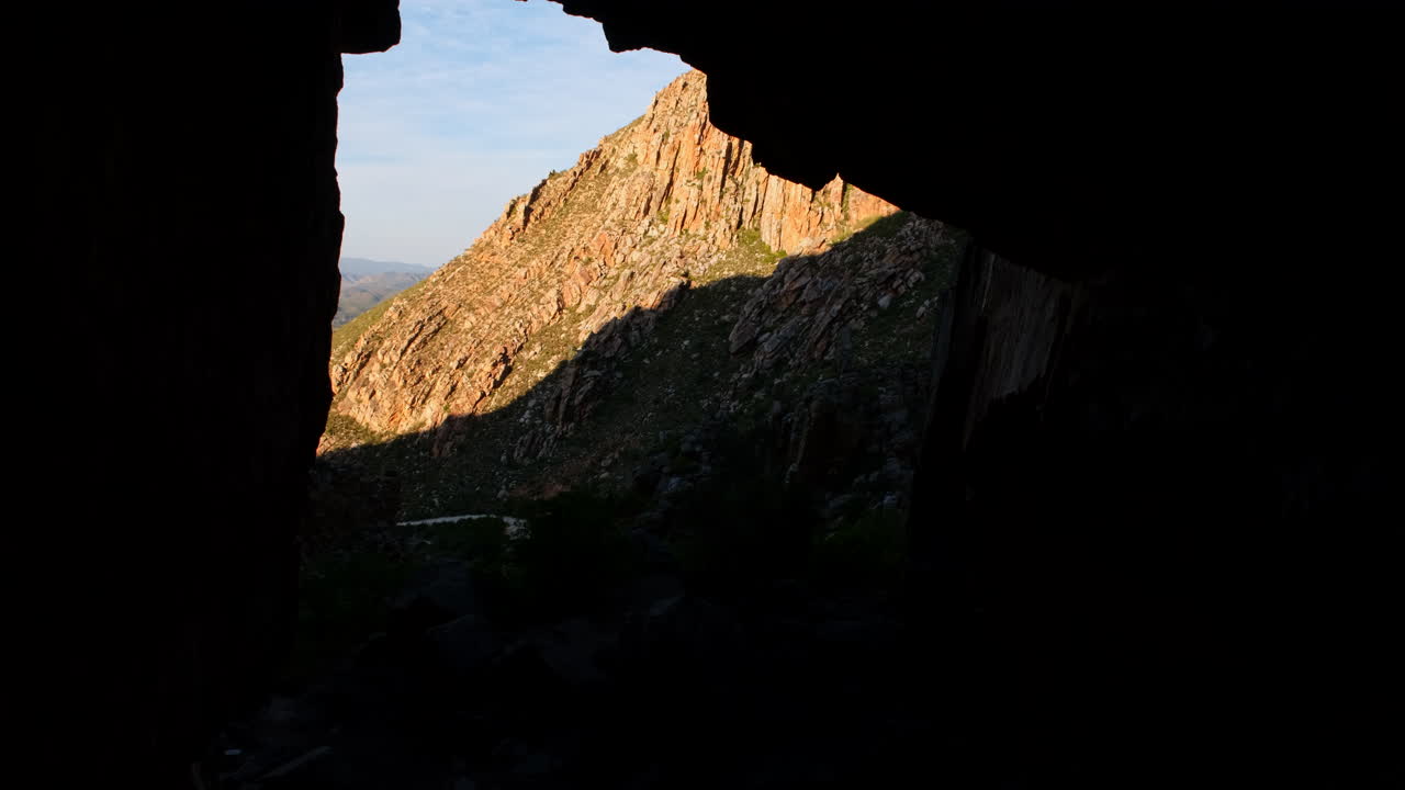 View from within dark cave of rugged mountainside at sunset, South Africa