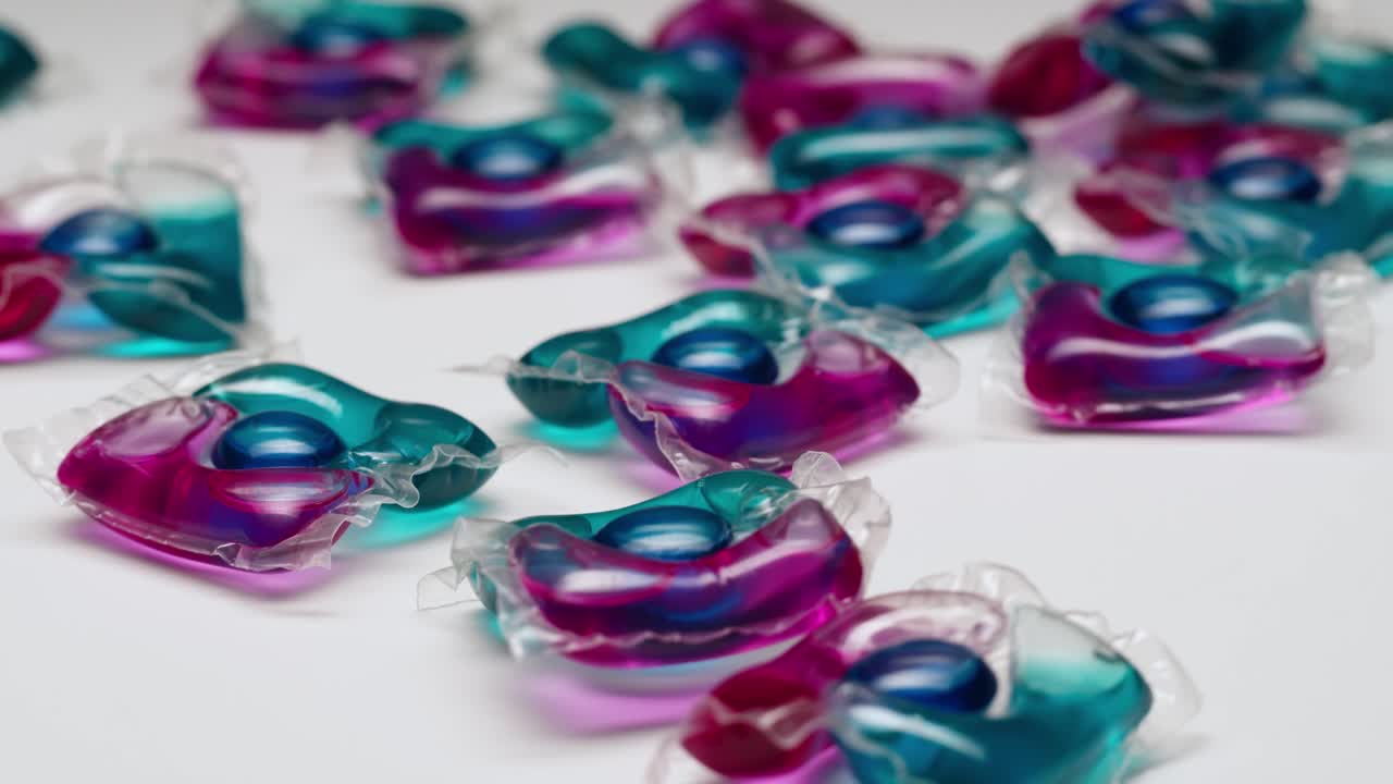Cápsulas de detergente para ropa de colores esparcidas sobre fondo blanco