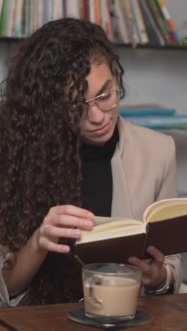 young woman reading and drinking coffee in a library