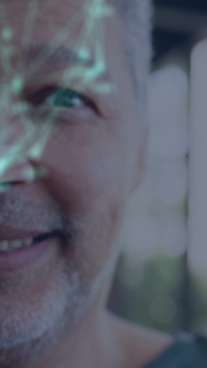 Video verticale: Uomo anziano che apre l'occhio sinistro e sorride mentre una luce verde a tema rete gli illumina il viso, per la tecnologia.