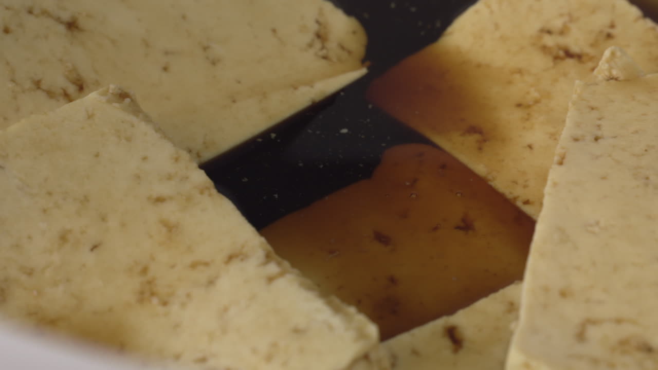Sliced Tofu Marinated In A Plastic Bowl With Soy Sauce And Garlic Powder - closeup shot