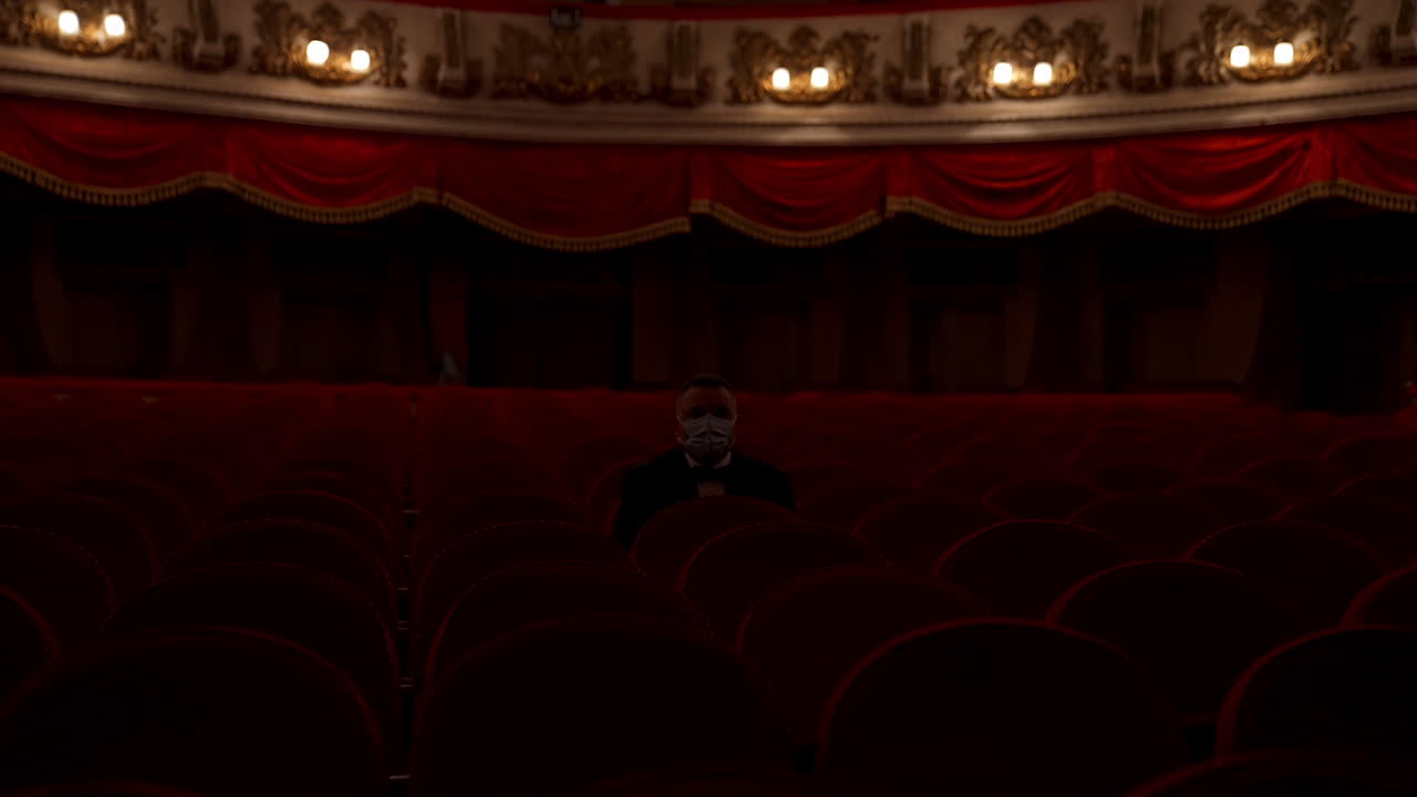 Man stands up from a red theater chair and throws medical mask away. Visitor in empty hall. Stop pandemic concept.
