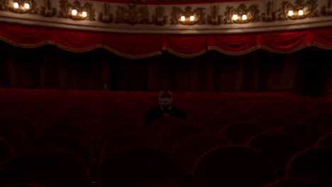 man stands up from a red theater chair and throws medical mask away. visitor in empty hall. stop pandemic concept.